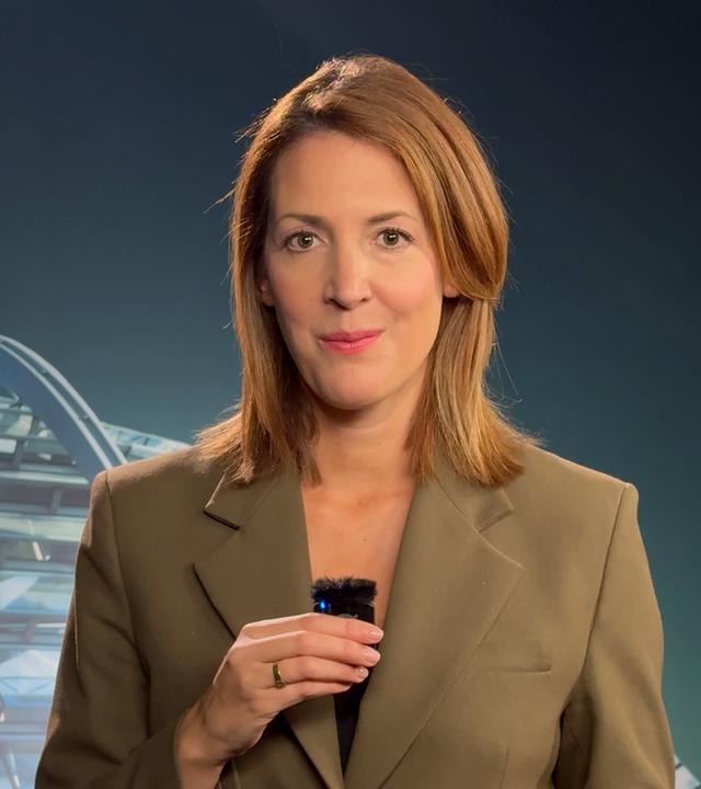 ZDF-Hauptstadtkorrespondentin Andrea Maurer trägt einen Khaki-farbenen Anzug. Sie steht in einem gut beleuchteten ZDF-Nachrichten Studio.