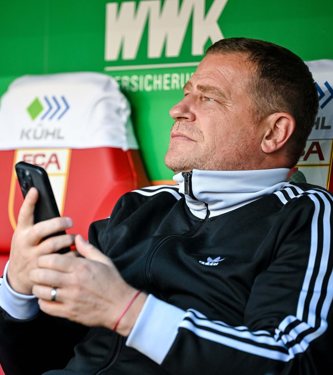 Max Eberl, Sportvorstand FC Bayern München, sitzt vor dem Spiel mit dem Handy auf der Bank.