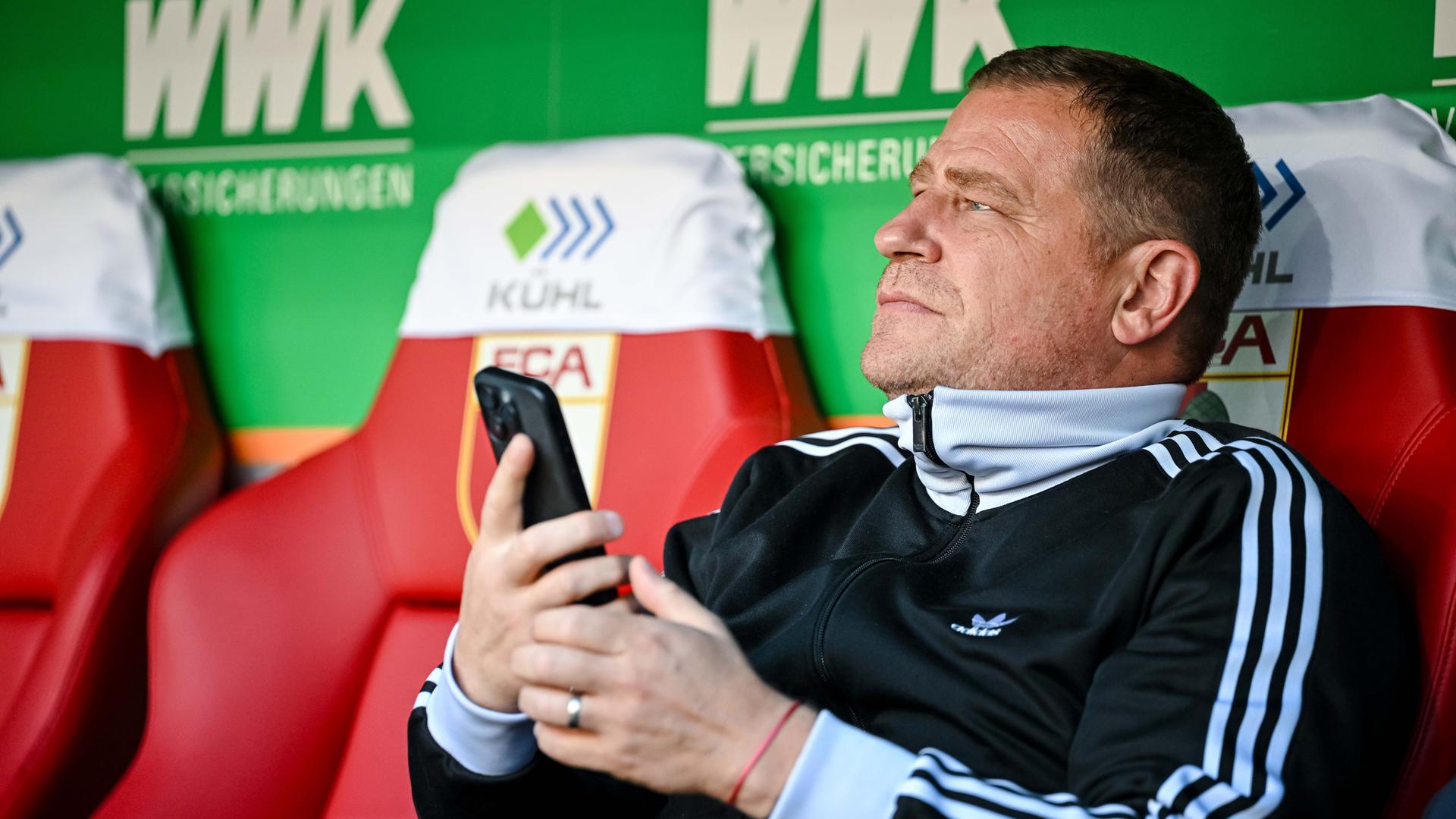 Max Eberl, Sportvorstand FC Bayern München, sitzt vor dem Spiel mit dem Handy auf der Bank.