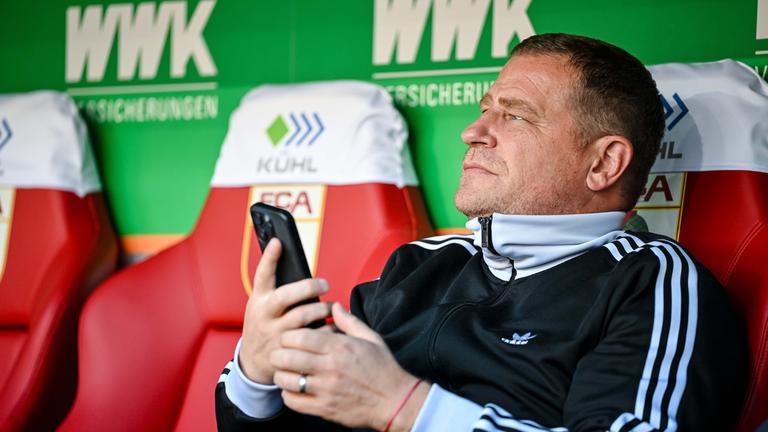 Max Eberl, Sportvorstand FC Bayern München, sitzt vor dem Spiel mit dem Handy auf der Bank.