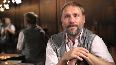Das Bild zeigt den Schauspieler Max Riemelt, der sich während eines Interviews über eine Stuhllehne stützt.
