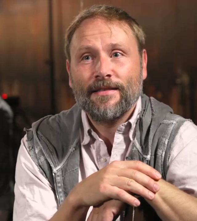 Das Bild zeigt den Schauspieler Max Riemelt, der sich während eines Interviews über eine Stuhllehne stützt.