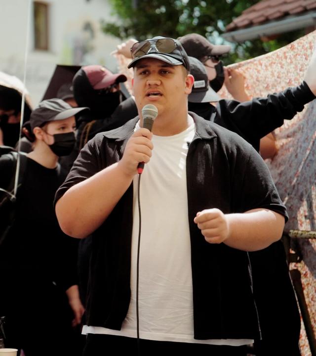 Aktivist Max Schneller spricht vor einer Gruppe Menschen in ein Mikrofon.