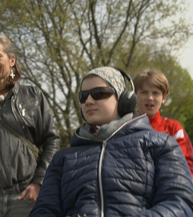 ME/CFS-Patientin Kalea mit Sonnenbrille und Gehörschutz im Rollstuhl