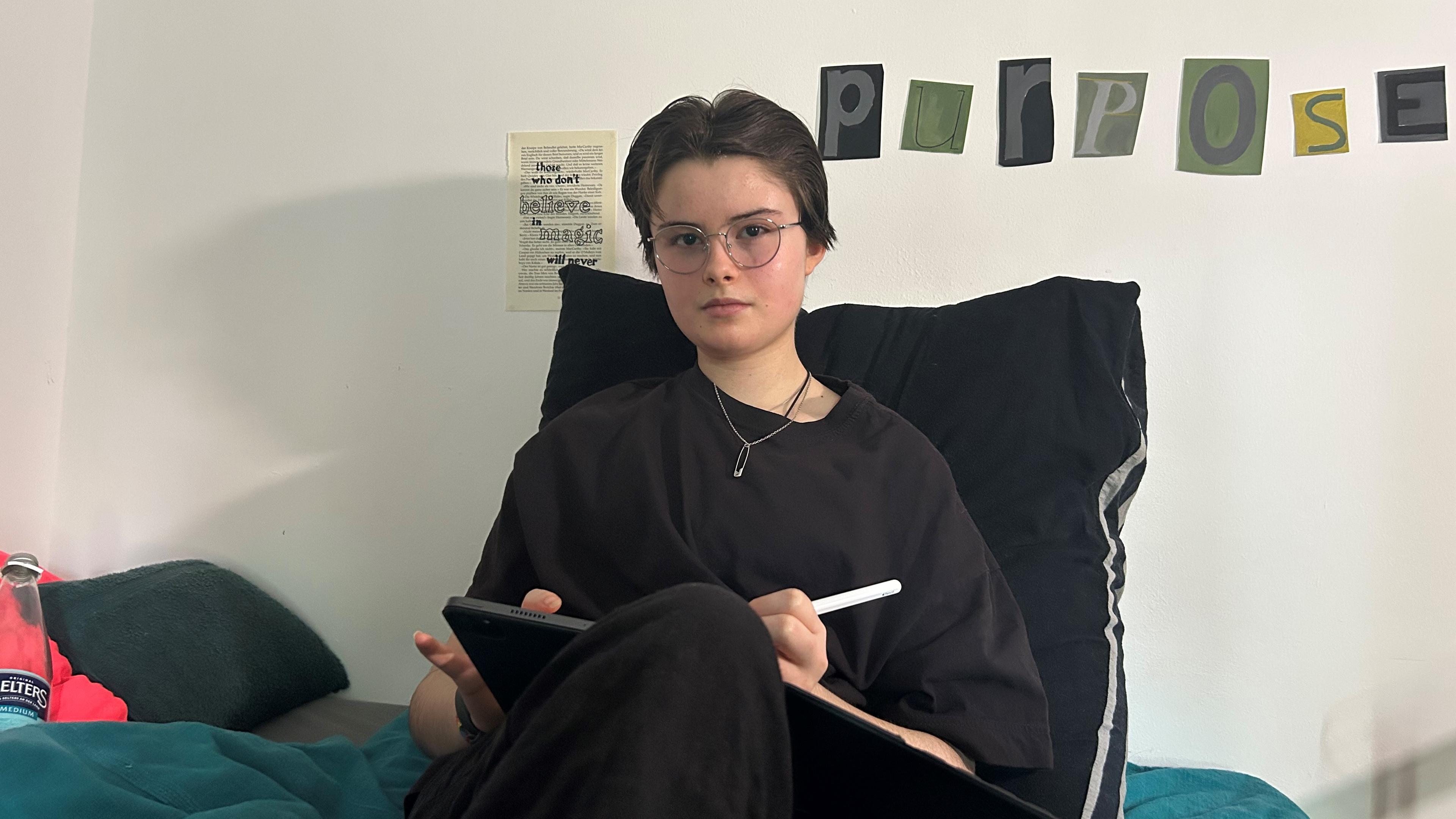 Die 13-jährige Lori sitzt mit einem Tablet auf ihrem Bett. Lori hat Myalgische Enzephalomyelitis/Chronisches Fatigue Syndrom (ME/CFS).