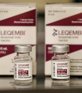 Das Medikament Leqembi in Fläschchen. Im Hintergrund steht die Verpackung des Medikaments