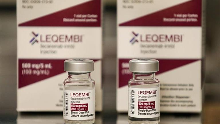 Das Medikament Leqembi in Fläschchen. Im Hintergrund steht die Verpackung des Medikaments
