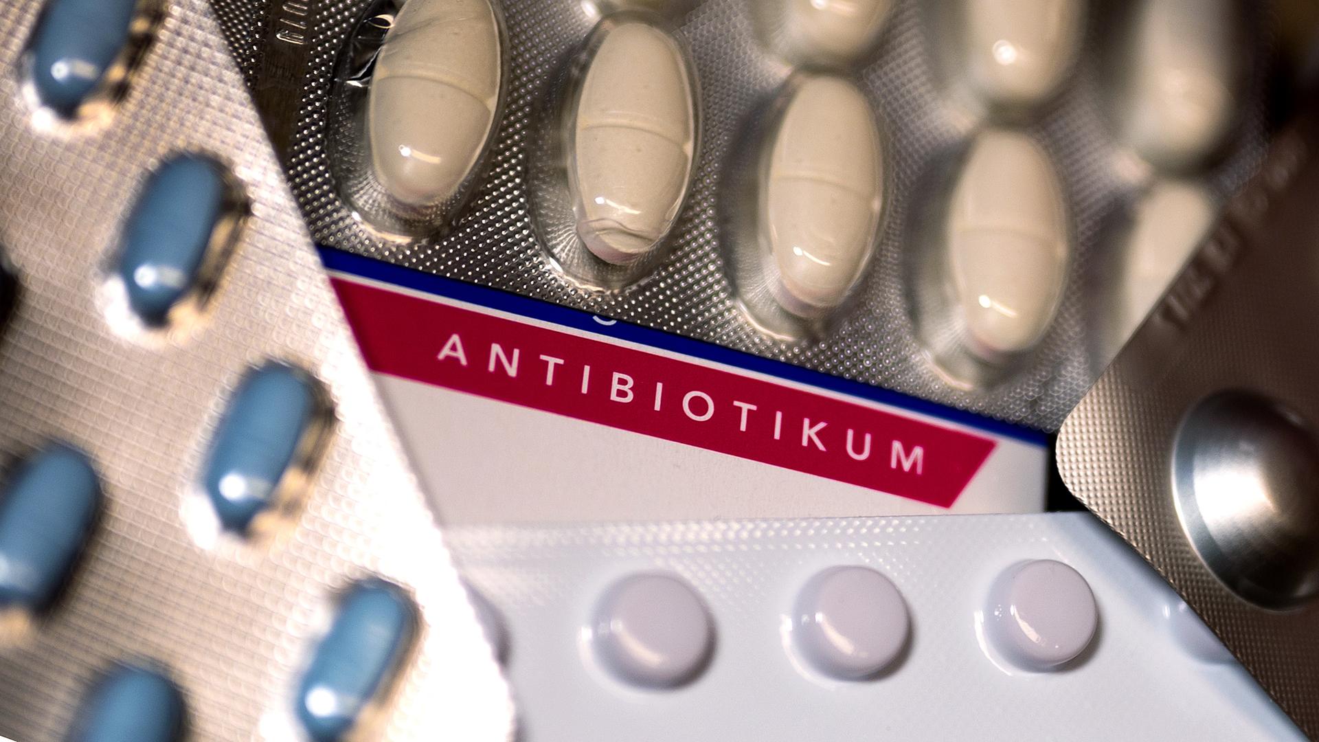 Mehrere Blister mit Tabletten und Pillen überdecken eine Packung mit der Aufschrift "Antibiotikum".