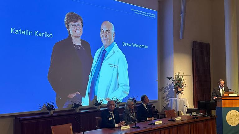 Fotos der Wissenschaftlerin Katalin Kariko und des Wissenschaftlers Drew Weissman sind bei der Bekanntgabe des Nobelpreises für Medizin auf einer Leinwand zu sehen.