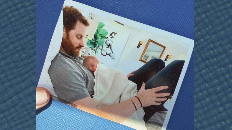 Ein Baby liegt auf dem Bauch von Prinz Harry.