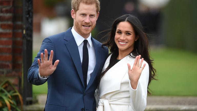 Meghan Markle und Prinz Harry winken in Richtung Kamera.