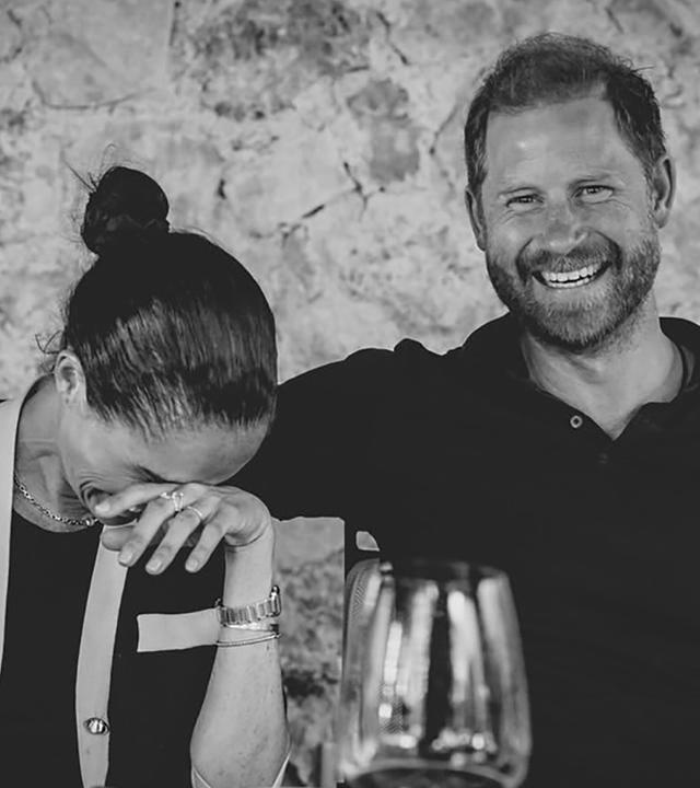 Meghan (links) und Harry sitzen an einem Tisch und lachen. 