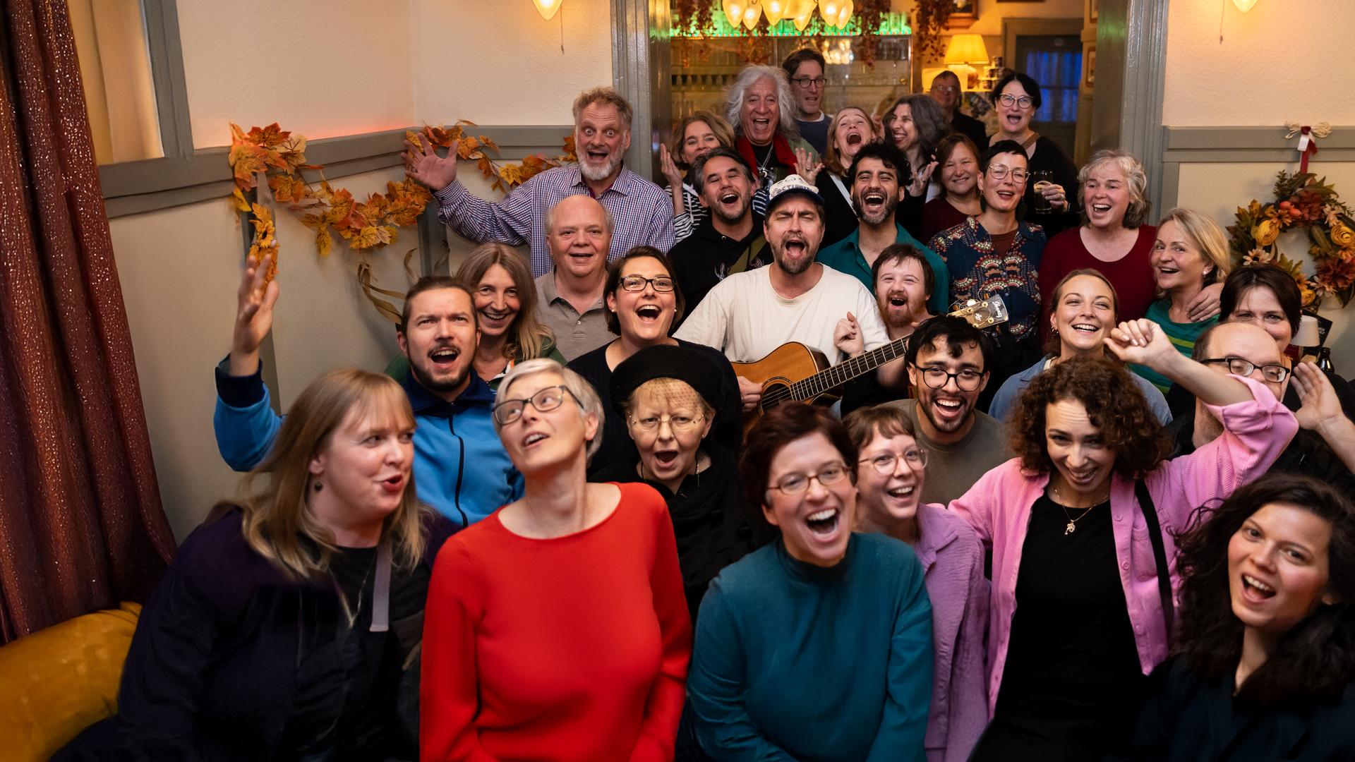 Eine Gruppe befindet sich singend in einem Wirtshaus, in der Mitte David mit Gitarre, Halbtotale.