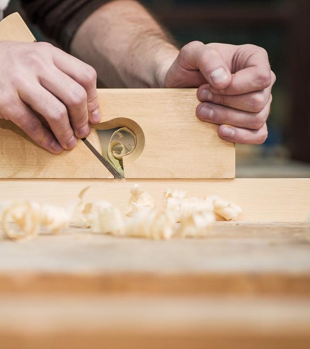 Ein Auszubildender arbeitet in der Holzwerkstatt mit einem Handhobel.