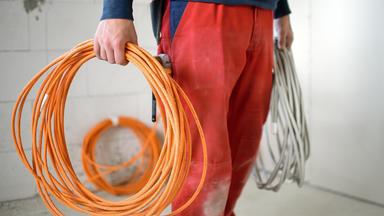 Ein Elektroniker-Lehrling arbeitet auf einer Baustelle.