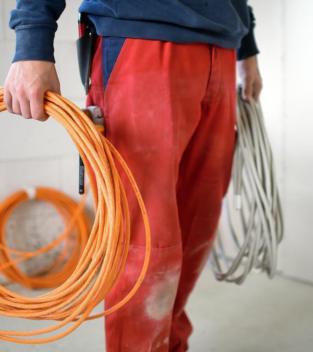 Ein Elektroniker-Lehrling arbeitet auf einer Baustelle.