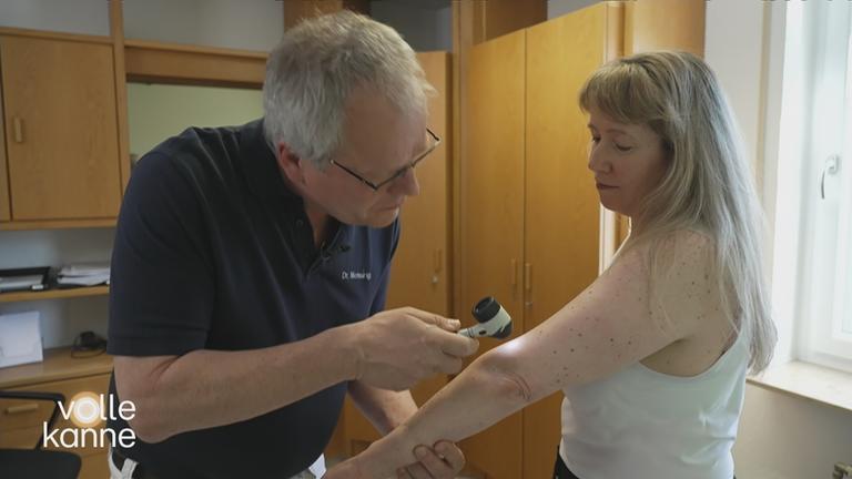 Ein Arzt untersucht mit einer Lupe eine Patientin auf Hautkrebs.