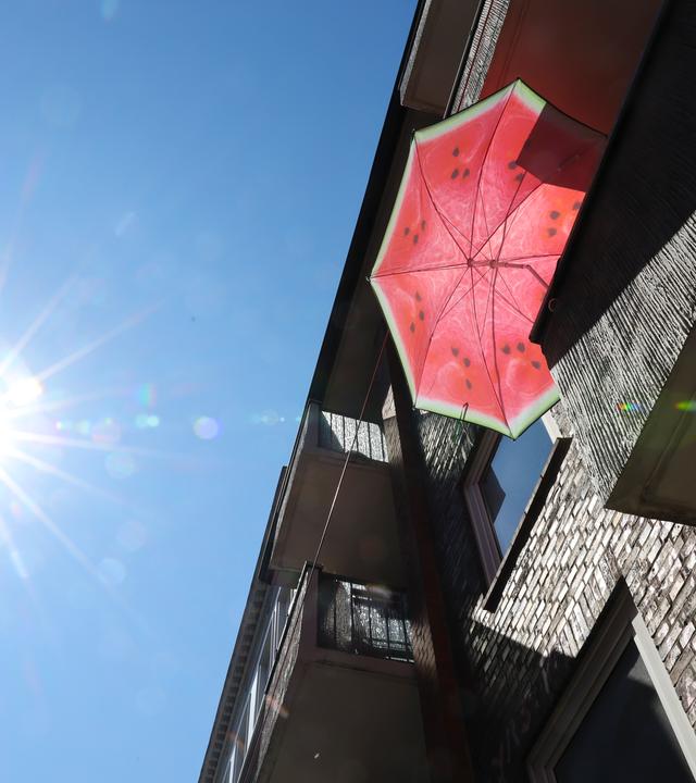 29.07.2026, Hamburg: Ein Sonnenschirm in den Farben einer Wassermelone steht auf einem Balkon.