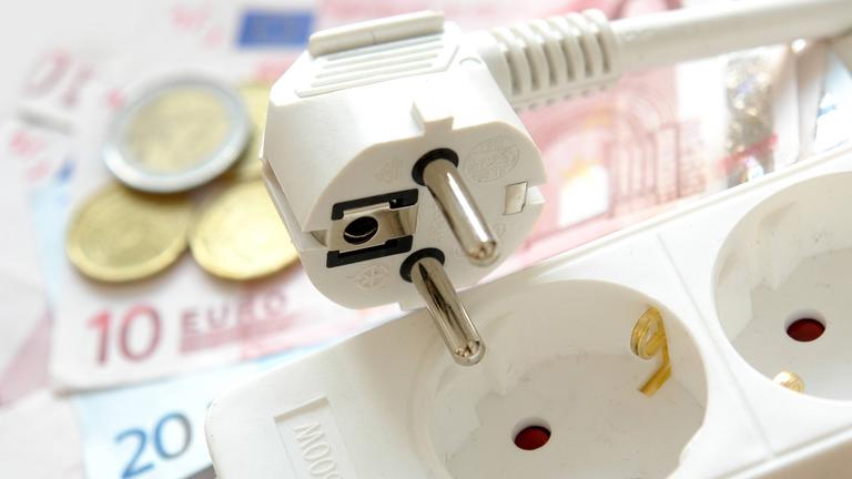 Mehrfachstecker mit Schalter, dahinter liegen Euros - als Symbolbild für Stromsparen.