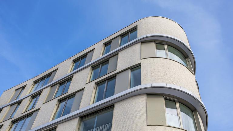 Ein modernes Mehrfamilienhaus mit großer Glasfassade und abgerundeten Ecken unter klarem blauen Himmel am 12.01.2026 in Tuttlingen.