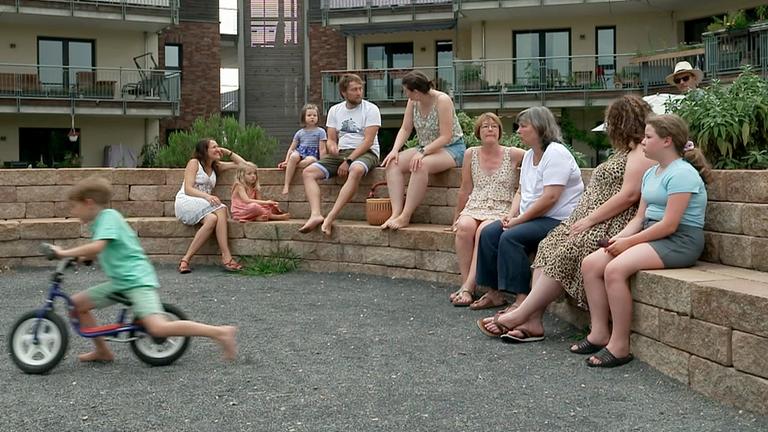 Mehre Menschen, jung und alt, sitzen im Innenhof einer Wohnanlage.