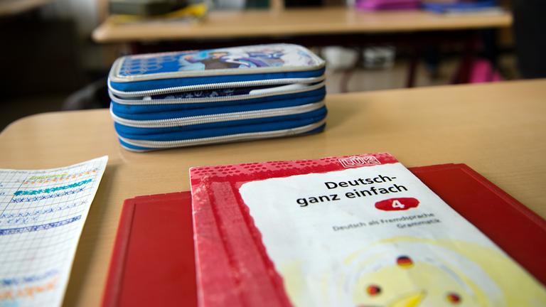 Es sind Schulsachen eines Kindes in der vierten Klasse zu sehen. Ein Federmäppchen und ein Schulbuch leigt auf dem Tisch