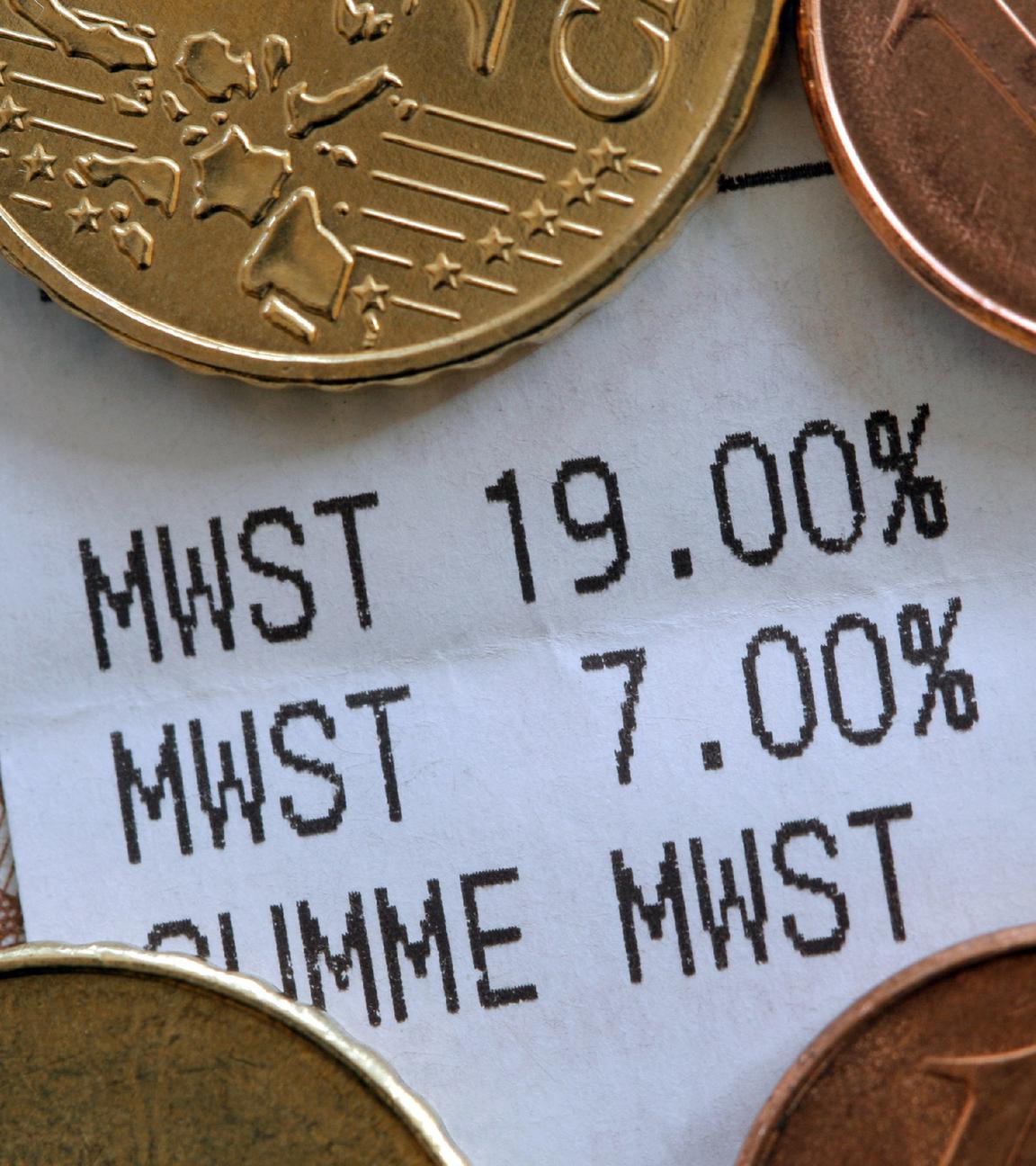 Ein Kassenbon mit unterschiedlichen Mehrwertsteuerangaben liegt unter Münzen.
