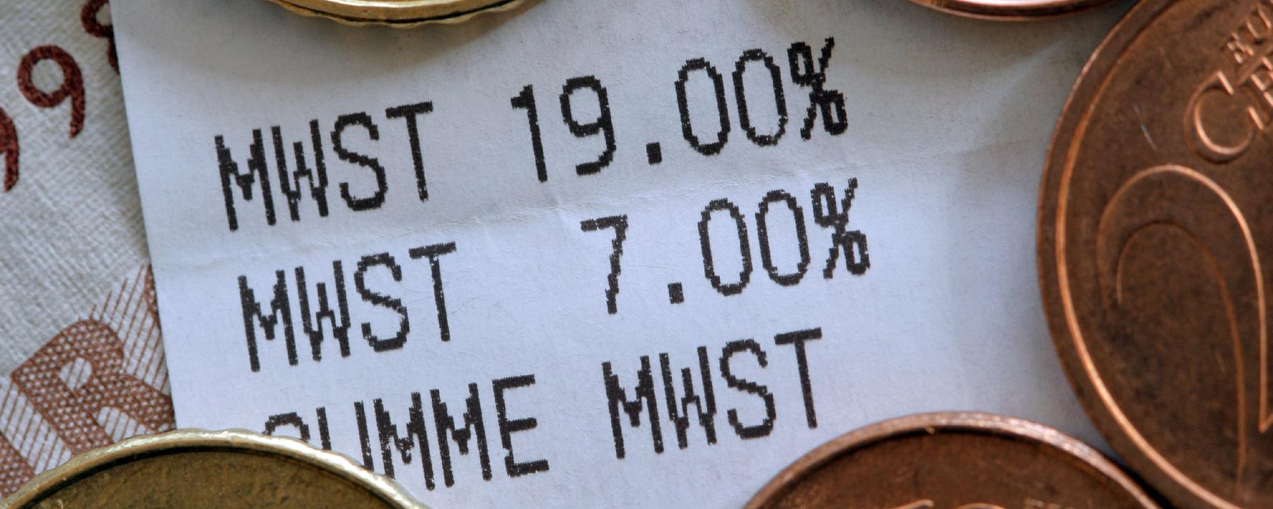Ein Kassenbon mit unterschiedlichen Mehrwertsteuerangaben liegt unter Münzen.