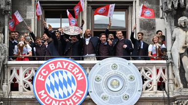 Die Spieler, Trainer und Betreuer vom FC Bayern München jubeln auf dem Rathausbalkon mit der Meisterschale am 17.05.2026 in München.