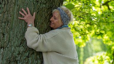Teilnehmerin Karin Bleischwitz umarmt im Kurpark einen Baum.