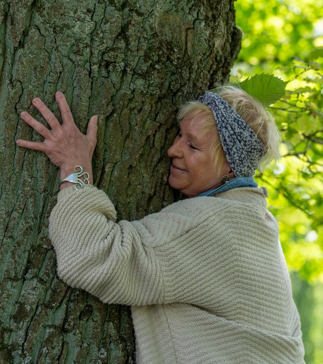Teilnehmerin Karin Bleischwitz umarmt im Kurpark einen Baum.