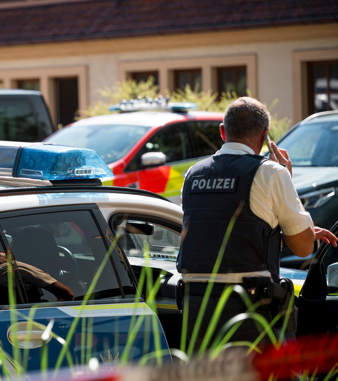 Ein Polizist steht an einem Polizeiauto. Ein 21-Jähriger hat in einer Firma in Unterfranken eine Kollegin getötet und zwei Männer schwer verletzt.