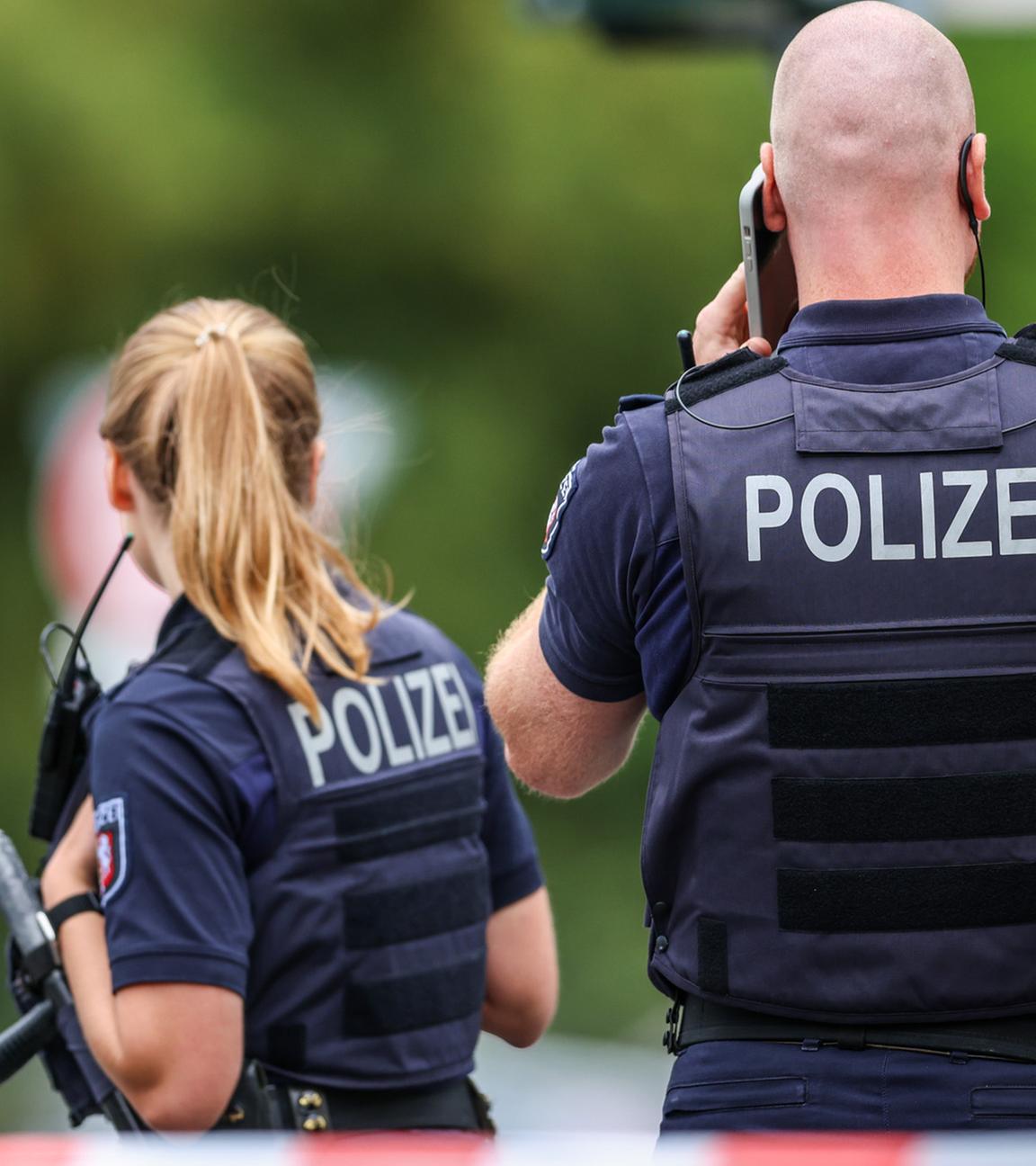 Polizeibeamte stehen zur Absicherung an einer Absperrung am Tatort. Nach Schüssen am 22.08.2025 in Menden im Sauerland ist die Polizei im Großeinsatz.