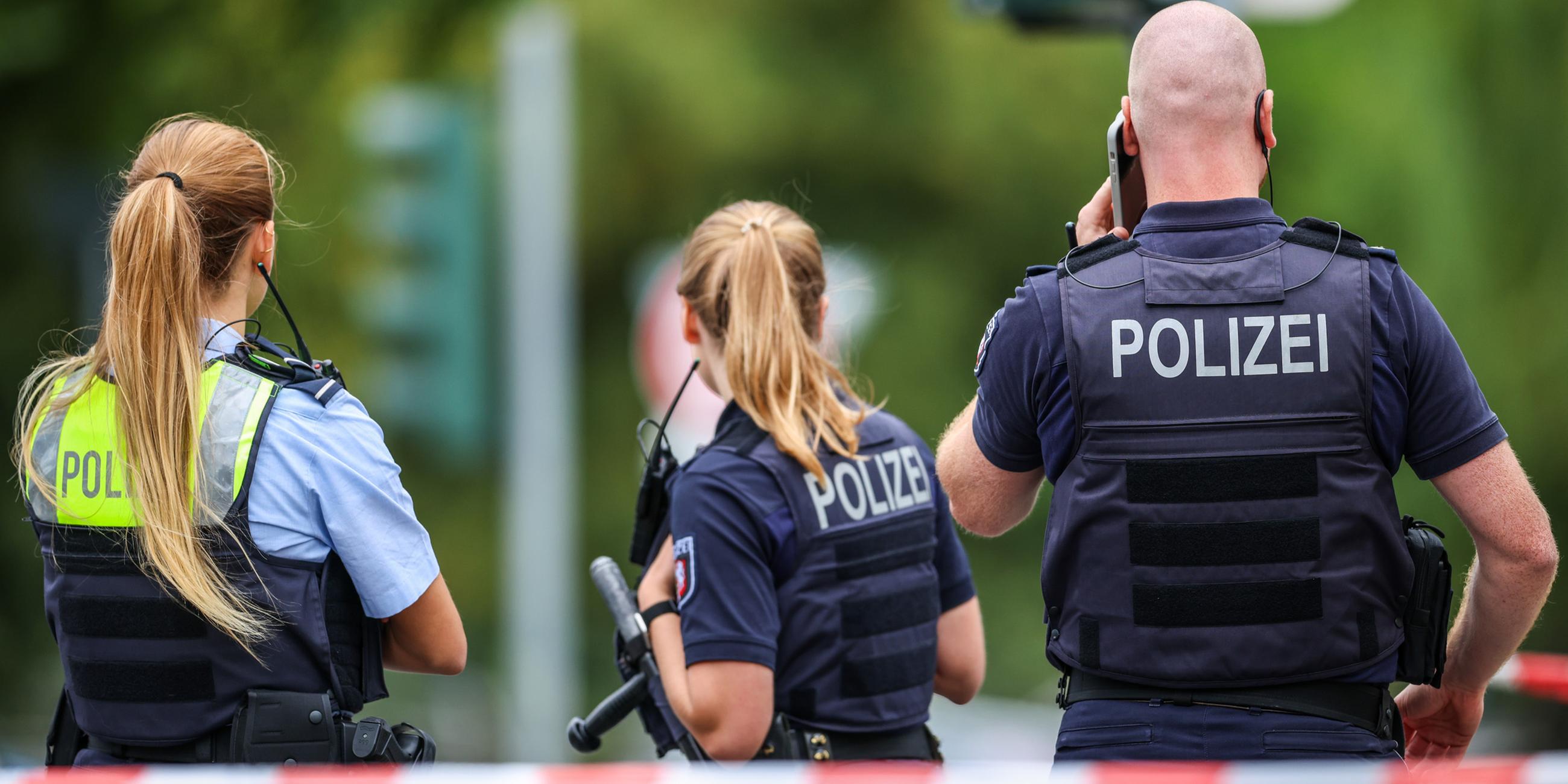 Polizeibeamte stehen zur Absicherung an einer Absperrung am Tatort. Nach Schüssen am 22.08.2025 in Menden im Sauerland ist die Polizei im Großeinsatz.