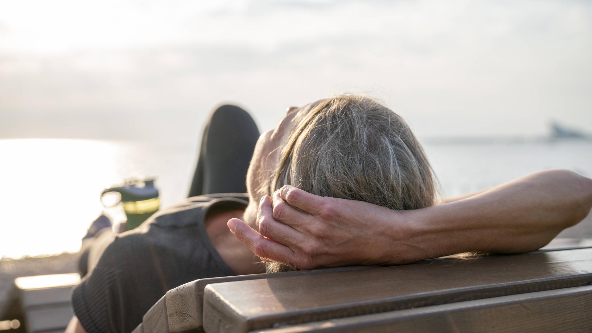 Reife Frau entspannt sich an einem sonnigen Tag auf einer Holzbank