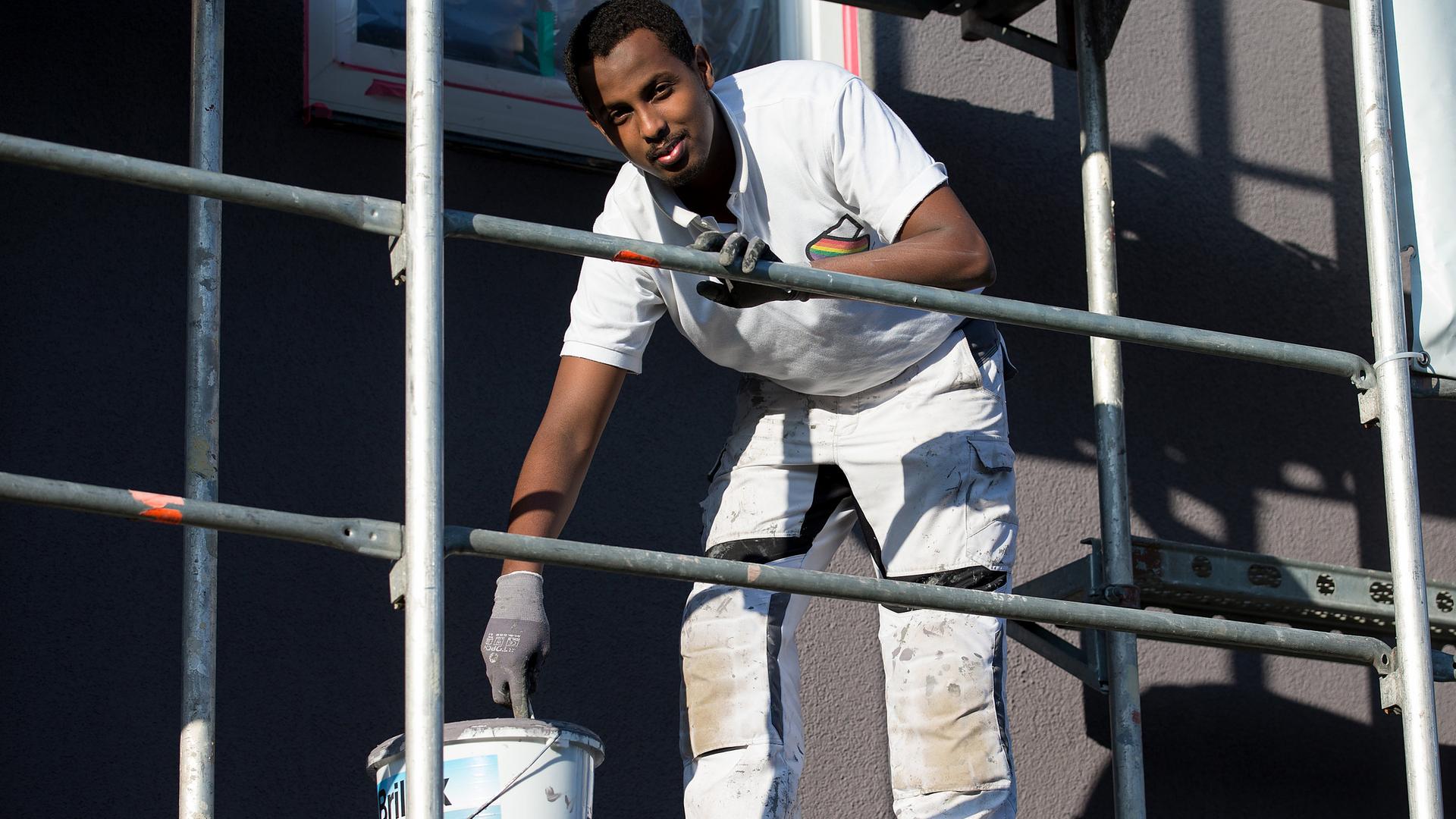 Der Auszubildende Ali Sharif steht mit Pinsel und Farbtopf am 27.10.2015 auf einer Baustelle in Osnabrück (Niedersachsen)