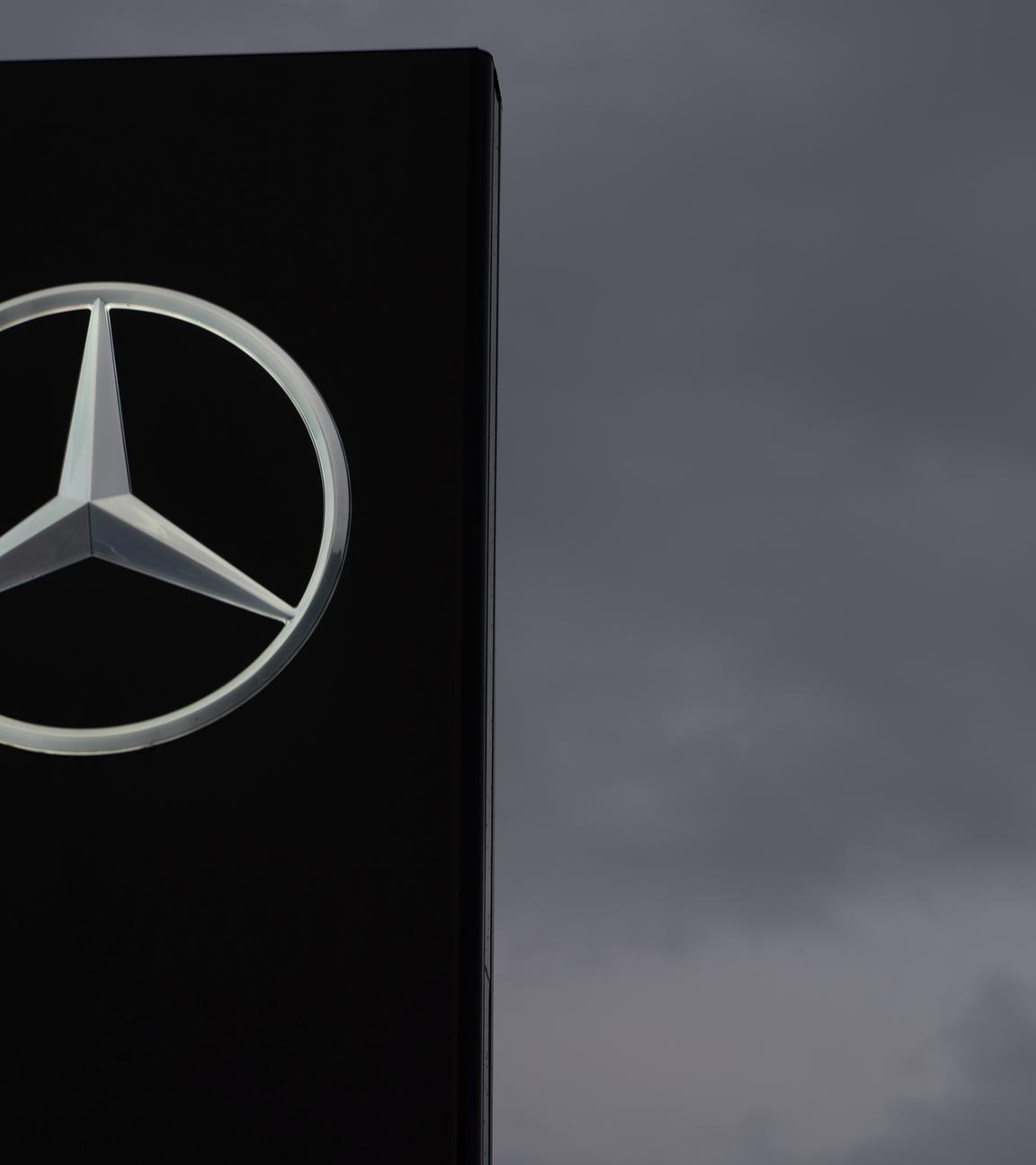 Ein Schild mit einem Mercedes-Stern ist vor einem grauen Himmel zu sehen. 