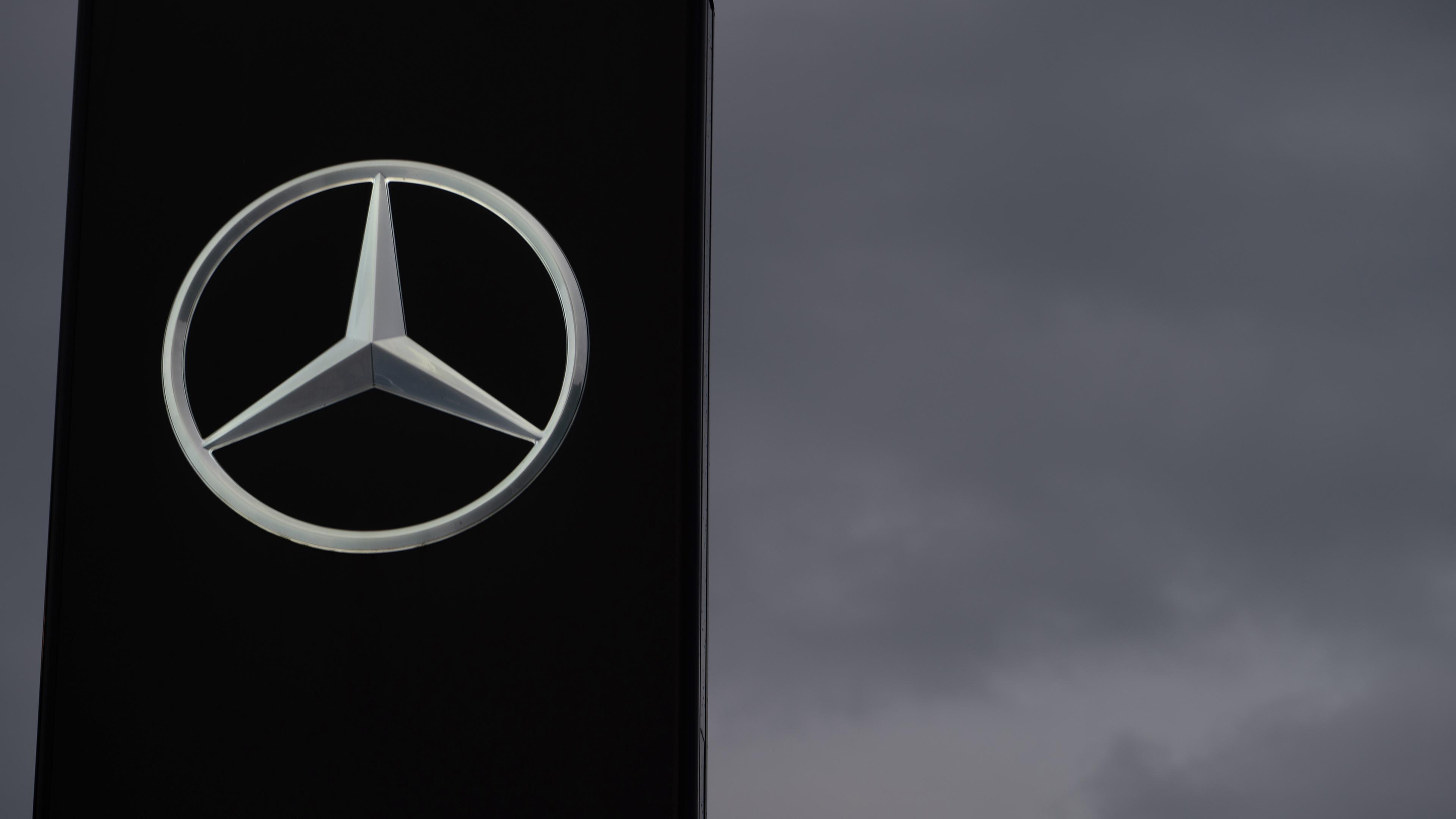 Ein Schild mit einem Mercedes-Stern ist vor einem grauen Himmel zu sehen. 