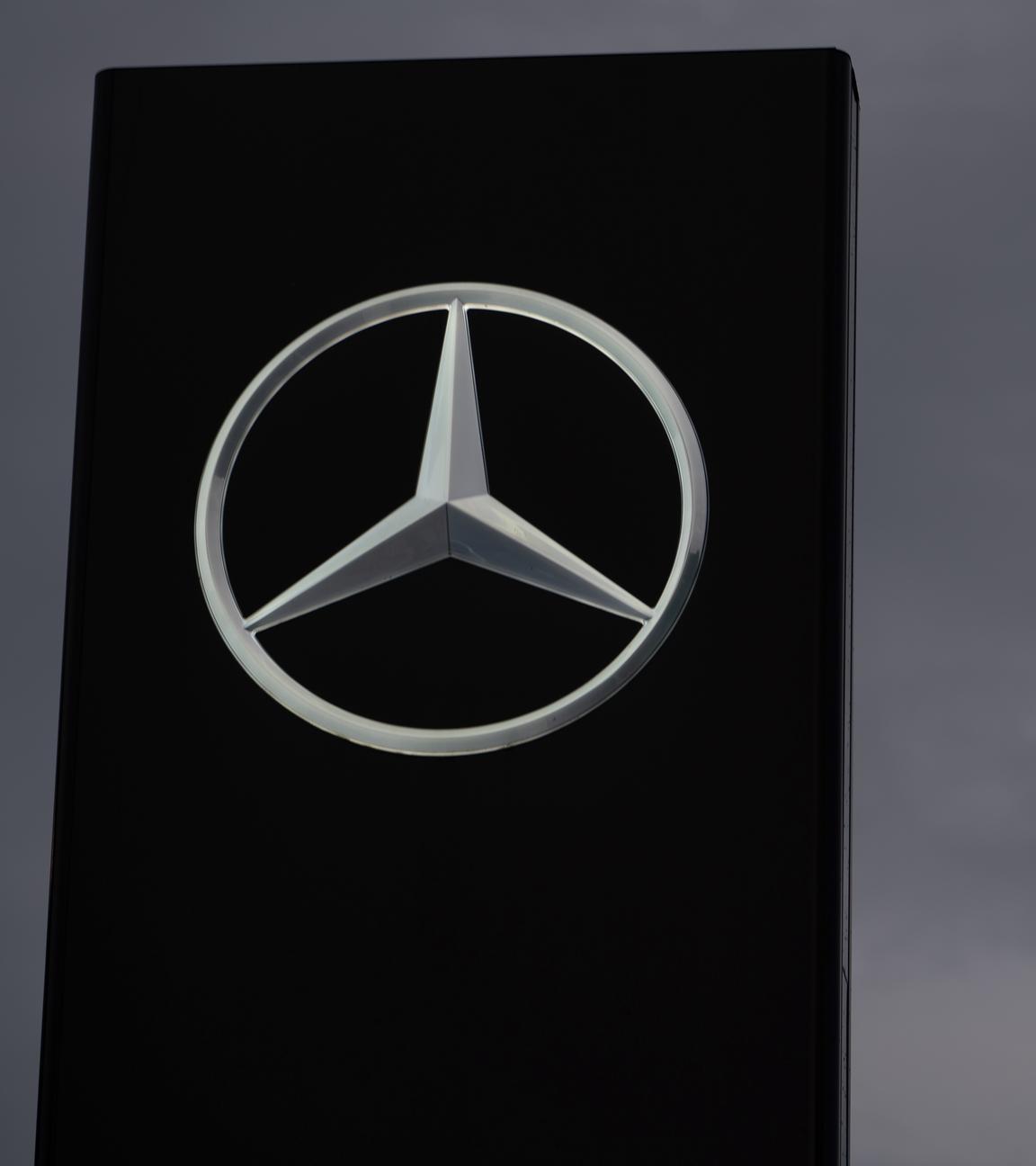 Ein Schild mit einem Mercedes-Stern ist vor einem grauen Himmel zu sehen.