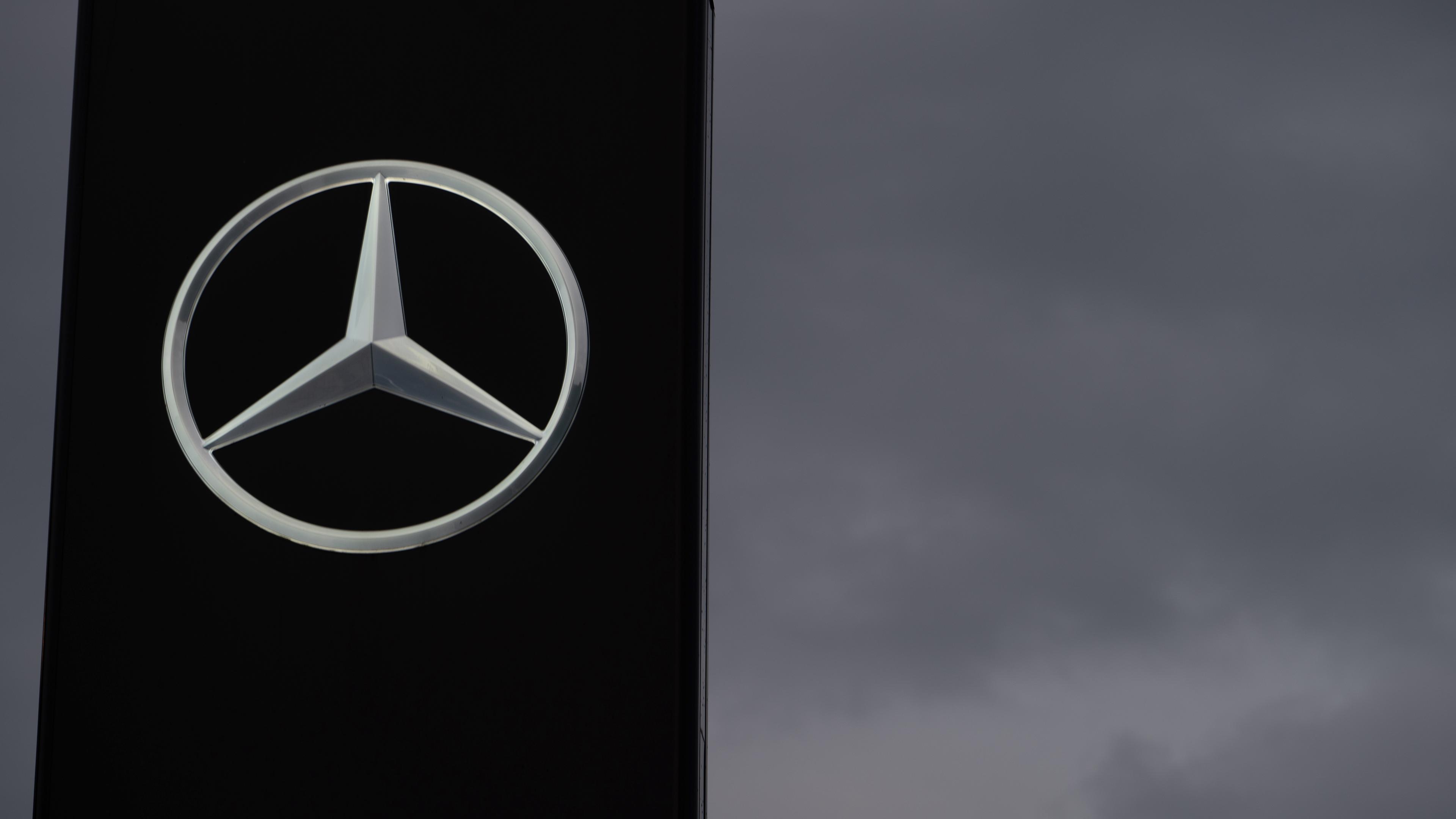 Ein Schild mit einem Mercedes-Stern ist vor einem grauen Himmel zu sehen.