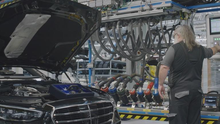 Arbeiter steht neben Mercedes mit geöffneter Motorhaube in Montagehalle 