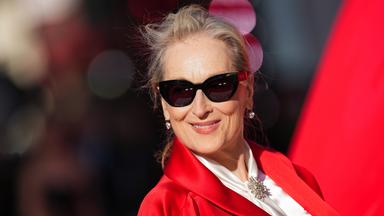Schauspielerin Meryl Streep in roter Jacke und Sonnenbrille auf einem roten Teppich.