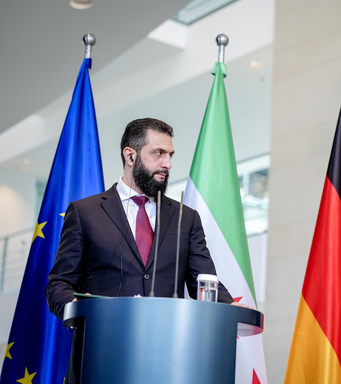 Syriens Übergangspräsident Ahmed al-Scharaa und Bundeskanzler Friedrich Merz stehen am Rednerpult bei der gemeinsamen Pressekonferenz im Bundeskanzleramt vor den Flaggen Deutschlands, Syriens und der EU.