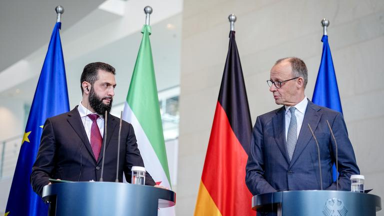 Syriens Übergangspräsident Ahmed al-Scharaa und Bundeskanzler Friedrich Merz stehen am Rednerpult bei der gemeinsamen Pressekonferenz im Bundeskanzleramt vor den Flaggen Deutschlands, Syriens und der EU.
