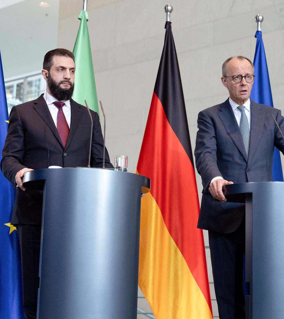 Friedrich Merz empfängt den syrischen Übergangspräsidenten: Ahmed al-Scharaa. Im Hintergrund stehen die syrische, die deutsche und die europäische Flagge