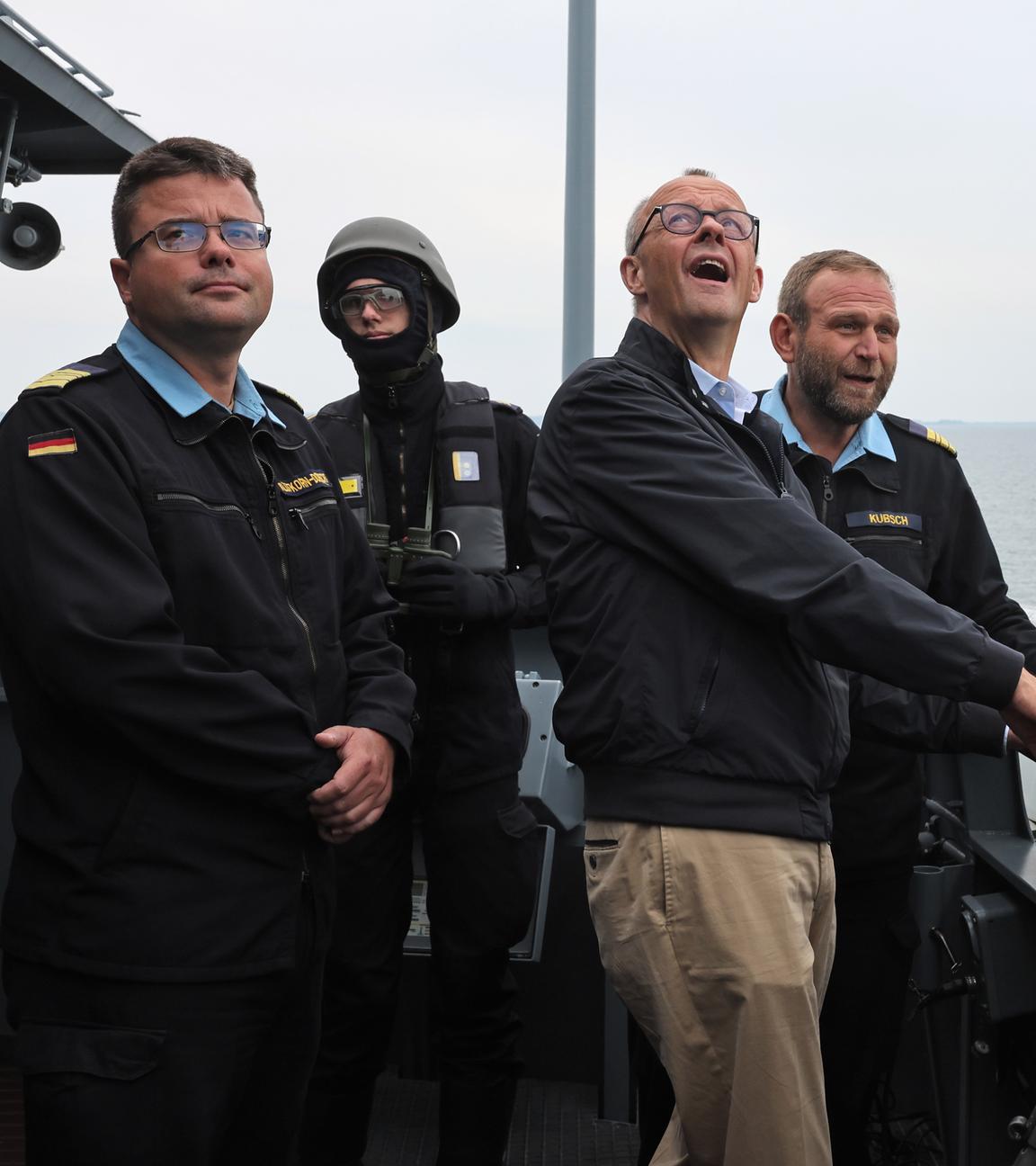 Bundeskanzler Merz steht mit weiteren Personen auf einem Schiff der Marine