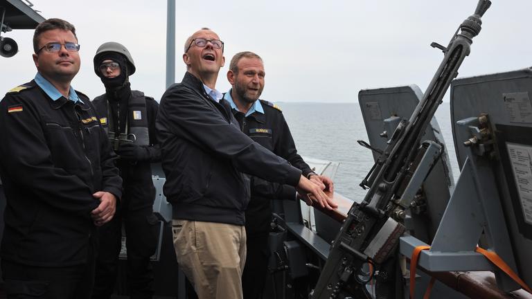 Bundeskanzler Merz steht mit weiteren Personen auf einem Schiff der Marine