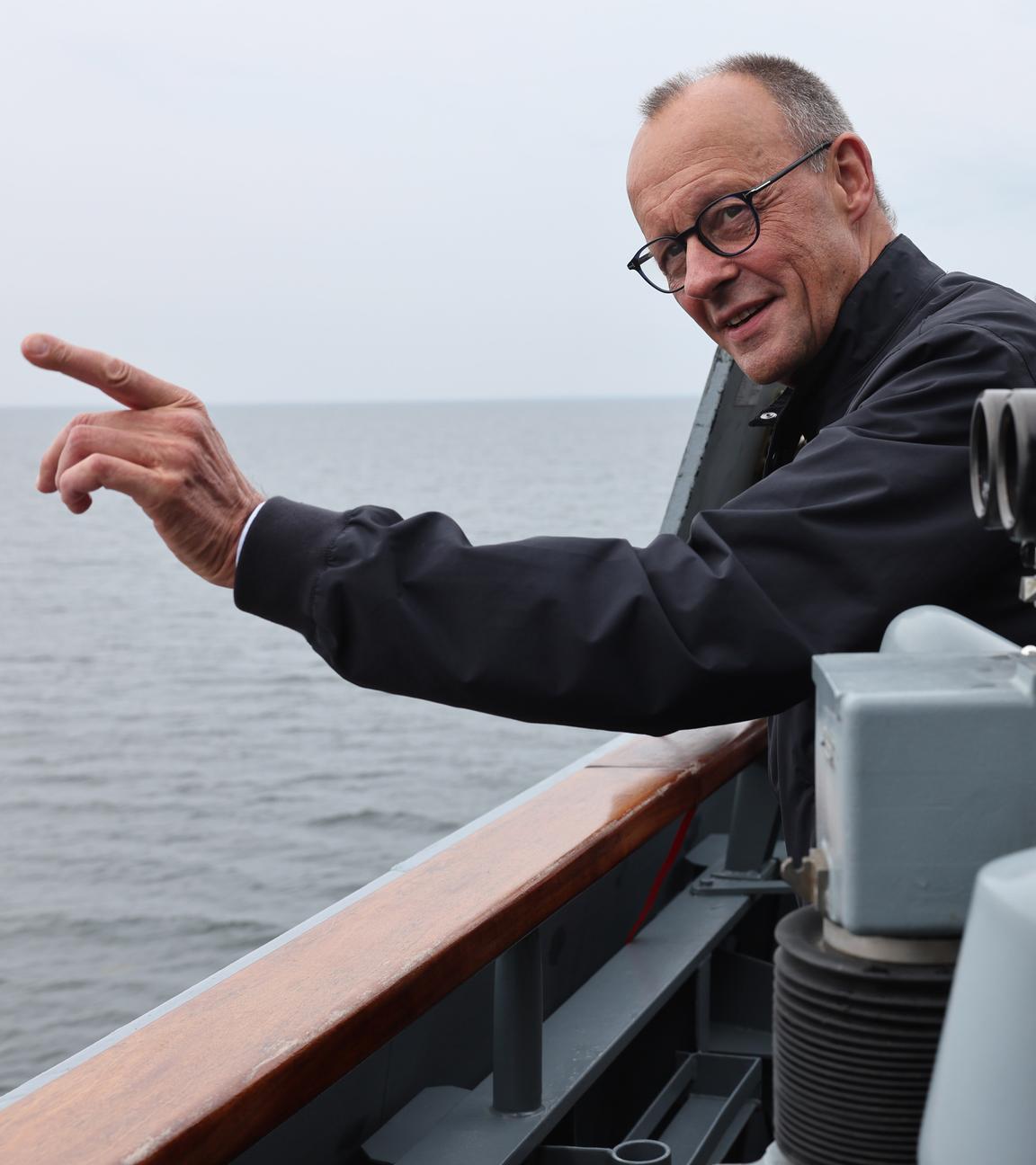 Merz ist auf einem Schiff der Marine. Er zeigt Richtung Meer und lacht.