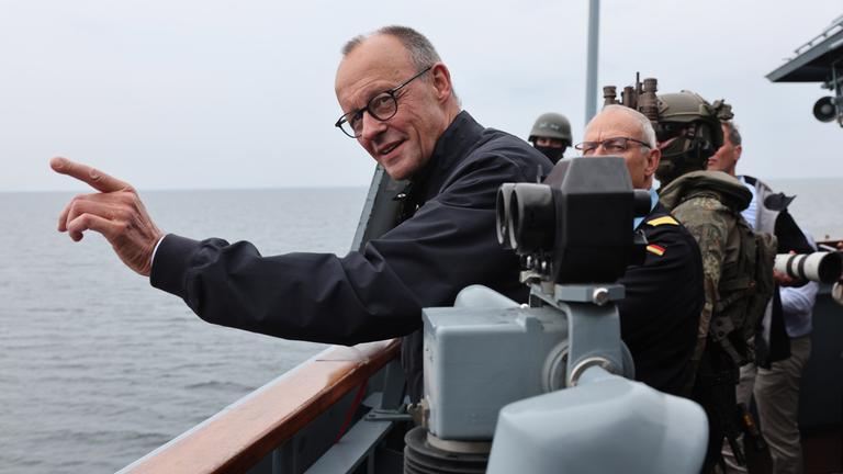 Merz ist auf einem Schiff der Marine. Er zeigt Richtung Meer und lacht.