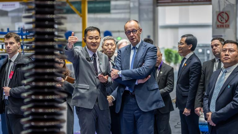 China, Hangzhou: Bundeskanzler Friedrich Merz (CDU) besucht die Firma Siemens Energy und wird von ZUang Wei, Siemens Energy China, Betriebsleiter, durch die Produktionshallen geführt.